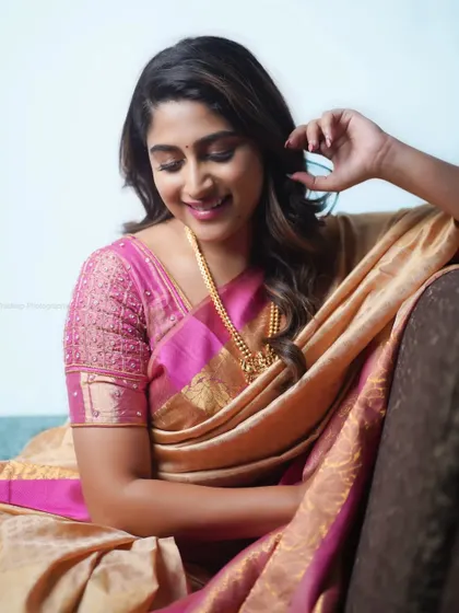 A beautiful portrait of actress Nishvika in a classic silk saree. The soft lighting and relaxed pose on the couch create a natural and elegant look.