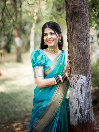 A classic outdoor portrait of the bride leaning against a tree, looking happy and radiant in her beautiful saree.