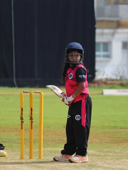 A young batter stands ready at the crease, learning the importance of concentration and a solid stance from an early age.