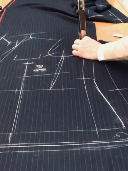 Precision in every cut. Our tailor uses traditional techniques to cut the fabric for a pinstripe suit, ensuring every pattern aligns perfectly for a seamless and professional finish.