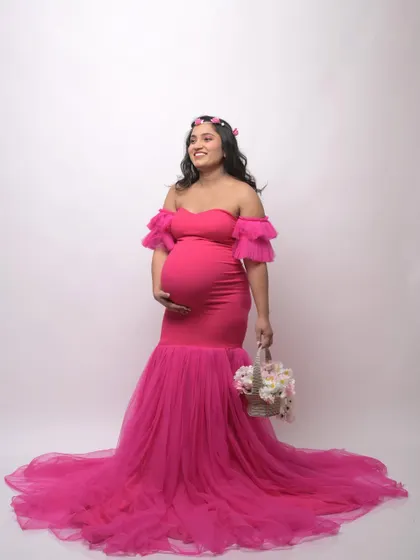 A full-length view of the popular hot pink mermaid gown. Accessorized with a flower crown and basket, this studio photo shows how you can personalize your maternity shoot style.
