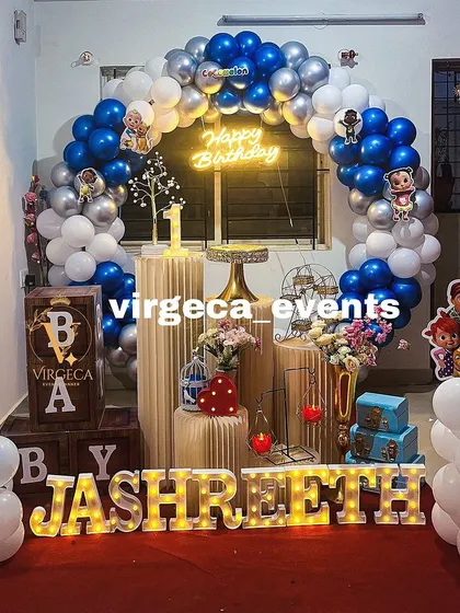 A fun and colorful Cocomelon theme for a first birthday. The setup includes character cutouts, a vibrant balloon arch, and marquee letters spelling out the birthday boy's name.