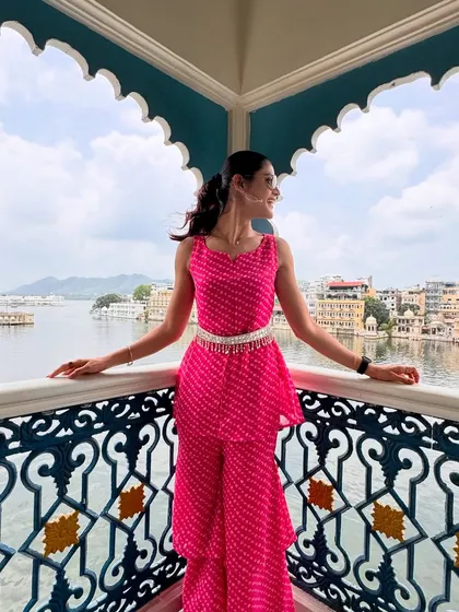 Another view of my pink bandhani outfit in Udaipur. The design of the balcony at The Leela Palace provides a perfect frame, highlighting both the outfit and the stunning view of Lake Pichola.