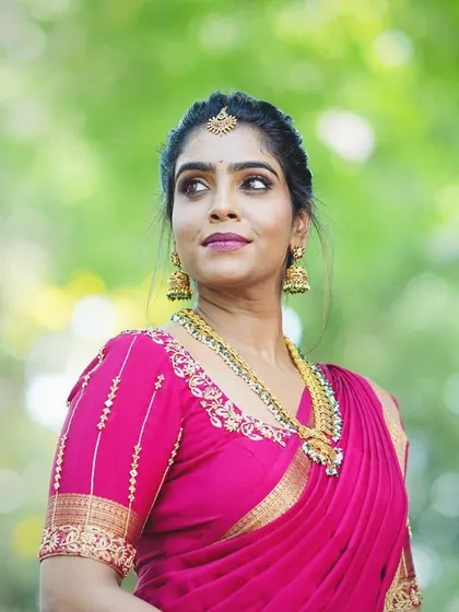A beautiful outdoor portrait of a bride in a vibrant pink silk saree. The natural light highlights the soft, glowing makeup and traditional gold jewellery.