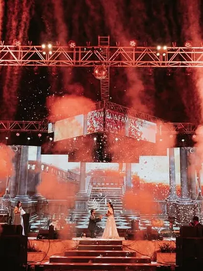 A grand, wide shot of a Sangeet stage with dramatic red lighting and fireworks, setting the scene for an epic night of performances.