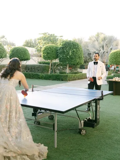 A fun, candid moment of Roha and Moin playing table tennis in their wedding attire in Dubai. It shows their playful personalities and the unique joy of their celebration.