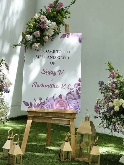 A welcome sign for a meet-and-greet event, framed by lush arrangements of purple and white flowers.