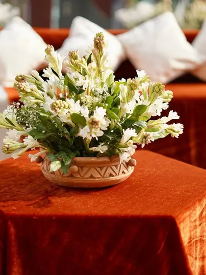 A delicate centerpiece of white tuberoses in a rustic woven basket, placed on a rust-colored velvet tablecloth, embodying understated charm.