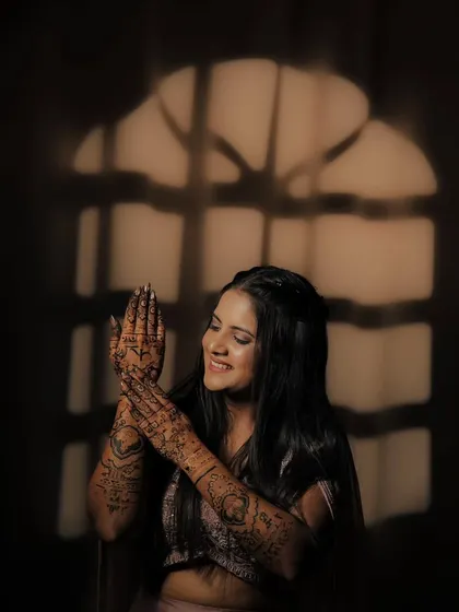 A happy bride admiring her mehandi in a beautifully lit setting. The window-like shadow adds a creative touch to the photo.