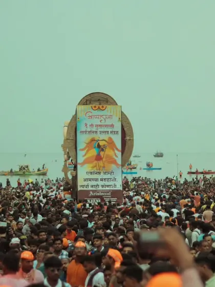A wide shot showing the sea of people gathered at the beach for the visarjan, with an idol and a large banner in the background. It truly captures the scale of the event.