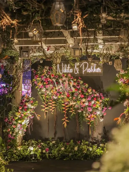 A view from within the floral tunnel, looking towards the neon sign. The use of rustic branches and hanging elements adds to the enchanted forest feel of the design.