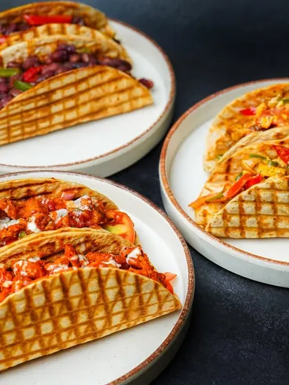 A delicious spread of assorted tacos, showcasing different fillings like paneer, chicken, and beans, served on three separate plates. This group shot captures the variety of a menu, making it a great choice for restaurant promotions.