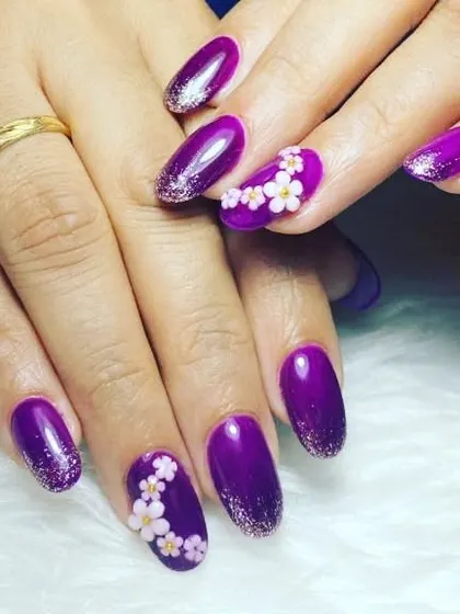 A royal purple manicure with a glittery ombre effect and delicate, hand-painted white flowers on accent nails.