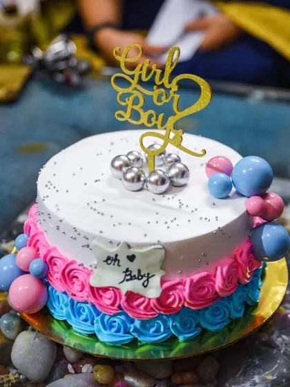 A close-up of a "Girl or Boy" gender reveal cake, beautifully decorated with pink and blue frosting roses.
