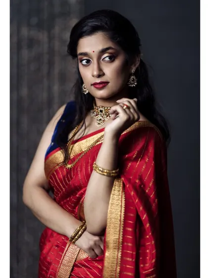 A classic three-quarter portrait against a dark, textured background. The model's confident gaze and the rich red of the saree make this a powerful and elegant image.