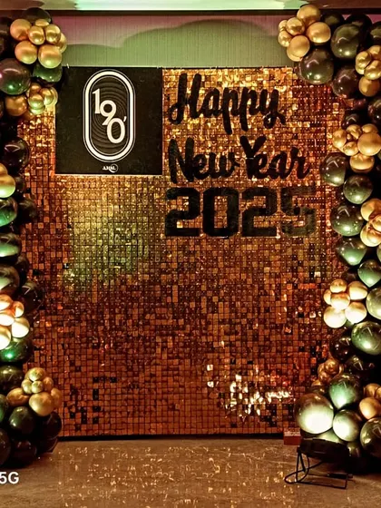 A New Year's party backdrop that also highlights the company brand. This design for '1o8' features their logo on a glittering gold sequin wall, framed by festive black and gold balloons.