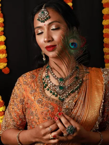 A creative portrait from a festive shoot. The makeup features soft, shimmery eyes and a bold red lip, with the peacock feather adding an artistic and traditional Indian element to the composition.