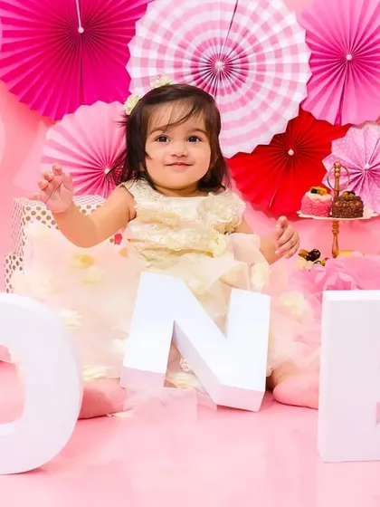 A happy baby girl sits among "ONE" blocks during her pink-themed first birthday, looking like a little princess.