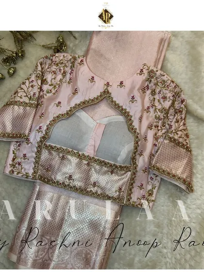 A pastel pink blouse with a unique back design featuring a temple-arch cutout. The sleeves are heavily embroidered with delicate floral motifs.