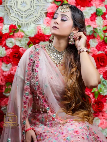 A beautiful portrait of a bride-to-be in her pastel pink lehenga, set against a wall of red and white flowers. A perfect shot from a ring ceremony or sangeet.