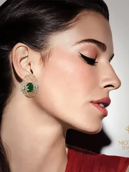A model wearing elegant stud earrings that combine the rich green of emerald with the sparkle of diamonds in a caged design. These are a sophisticated choice for any occasion.
