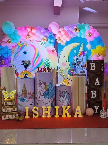Our unicorn theme is pure magic. This setup for Ishika's birthday features pastel unicorn illustrations on pedestals, a rainbow balloon arch, and light-up letters for an enchanting party.