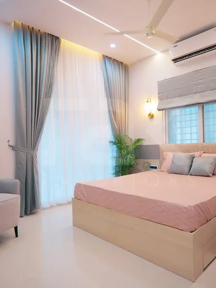 A serene bedroom with a soft color palette of pink, grey, and light wood. The combination of a comfortable armchair, elegant curtains, and warm lighting creates a perfect space for relaxation.