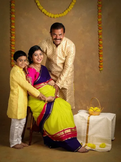 A happy family portrait celebrating their growing family. Dressed in coordinated yellow ethnic wear, they are all smiles as they lovingly hold the baby bump, surrounded by traditional marigold garlands.