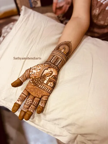 A traditional bridal design with a prominent peacock on the palm. The pattern includes classic elements like checkerboard fillers and floral bands, extending up the forearm.
