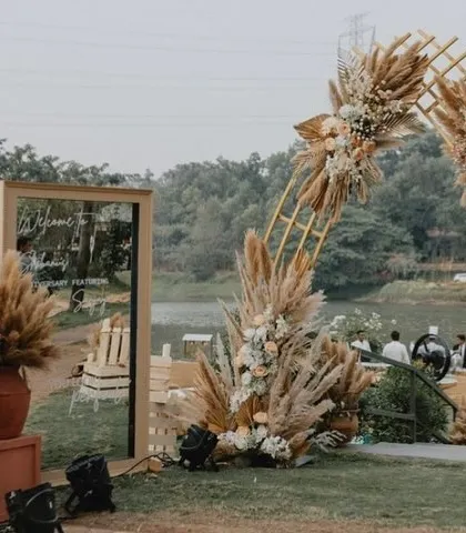 The entrance to a beautiful bohemian sundowner anniversary party, featuring a large pampas grass arch and a modern welcome mirror.
