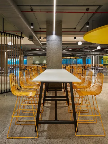 A high-top communal table with bright yellow wireframe stools. The industrial design is softened by the use of bold, cheerful color.