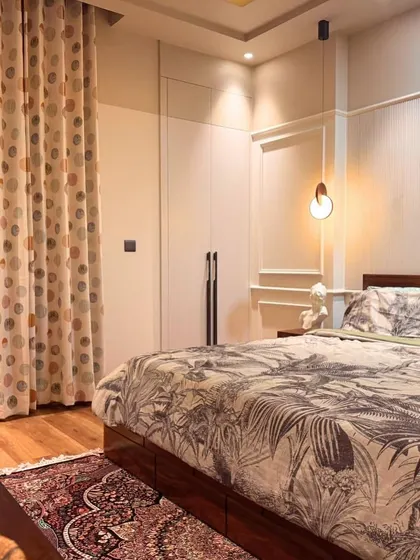 A view of the bedroom showing the patterned curtains that add a playful touch to the otherwise neutral and classic design. The built-in wardrobe provides ample storage.