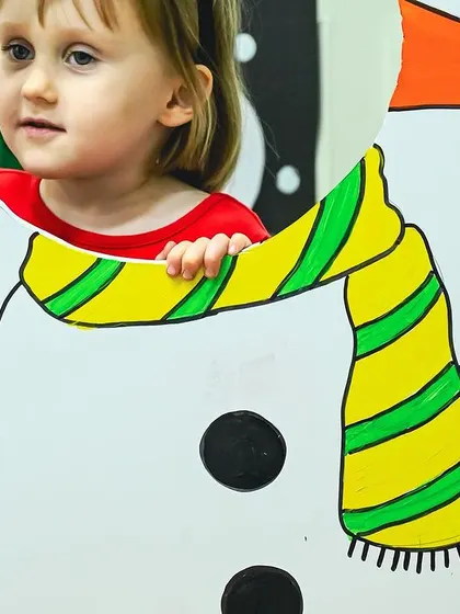 A child peeks through a snowman photo cutout, a fun prop at our Christmas party. I always include playful elements to make the events memorable.