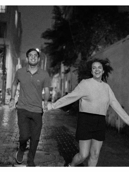 A black and white shot of a couple running hand-in-hand down a wet city street, full of joy and spontaneity.