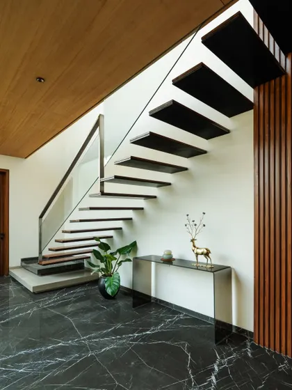 A floating staircase with a glass balustrade and dark marble flooring. The minimalist design maintains an open and airy feel in the foyer.