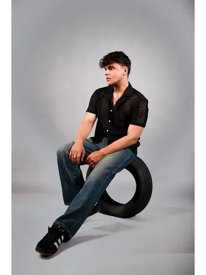 A male model in a casual black shirt and jeans, using a tire as a prop against a grey studio background. This adds an urban, slightly edgy feel to a standard lookbook photo.