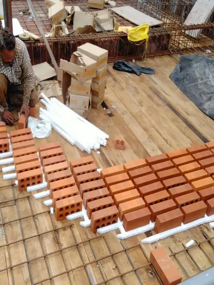 A mason carefully places perforated bricks according to the design for the exposed slab. This technique reduces the amount of concrete needed and creates a unique, textured ceiling finish.