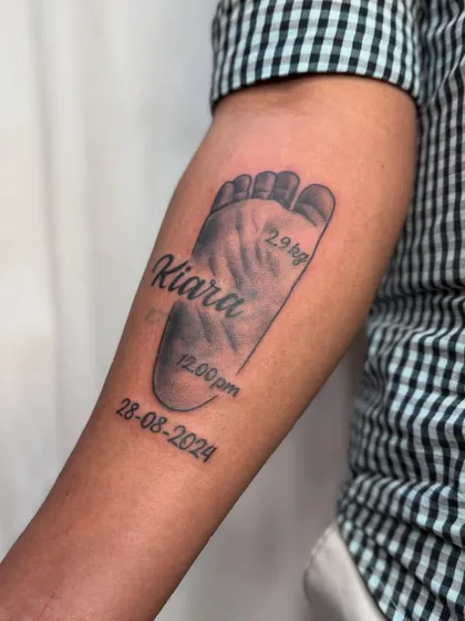 A clear, detailed shot of the baby footprint memorial tattoo on the forearm.