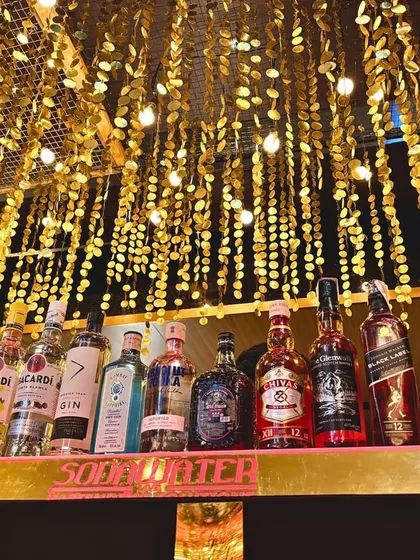 The bar area, with liquor bottles neatly arranged under a ceiling of shimmering gold discs, creating a luxurious and inviting atmosphere.