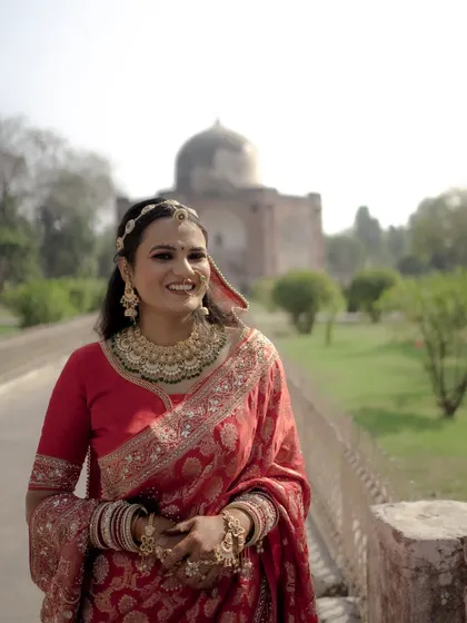 A stunning portrait of the bride in her red saree and magnificent gold jewelry, smiling brightly at her historic wedding venue.