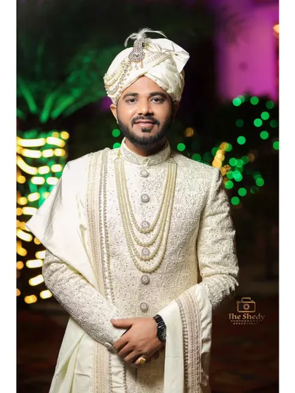 A classic portrait of the groom in his white sherwani and pearl necklace. He looks regal and ready for his wedding ceremony.