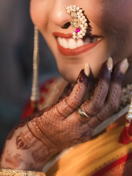 A close-up on the details: the beautiful smile, the traditional nath, and the intricate mehndi design. These shots celebrate the artistry of the bridal preparation.