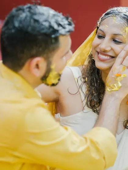 The groom gently applies haldi to the bride's cheek, a tender moment from their outdoor haldi ceremony.