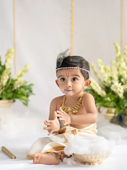 Our little Krishna enjoying his pot of butter. The all-white setup with fresh flowers creates a serene and divine atmosphere for this Janmashtami themed baby photoshoot.