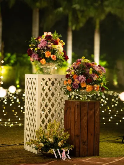 Floral arrangements on pedestals of different materials, one white lattice and one rustic wood. This mix-and-match approach adds visual interest and texture to the decor.