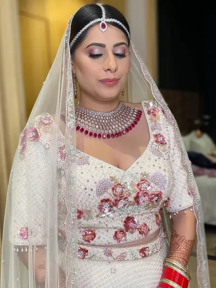 A subtle bridal glam look for a modern bride. The soft pink eyeshadow complements the ruby jewelry and the floral embroidery on her white lehenga.