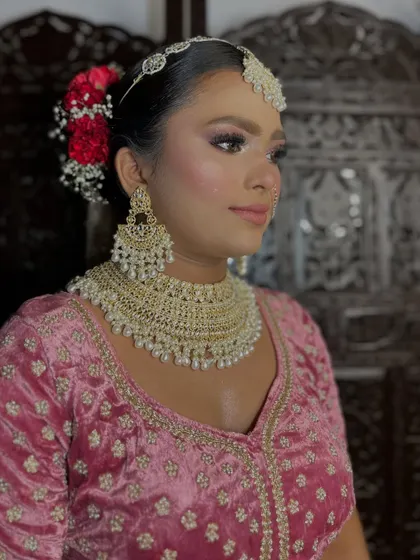 This side profile shows the elegant floral bun and the intricate details of the pearl jewelry, perfectly complementing her soft glam bridal makeup.
