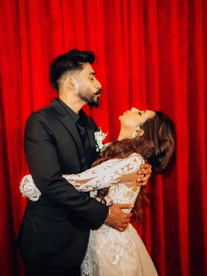 A playful and dramatic pose against a rich red curtain. This creative couple portrait adds a touch of theatrical flair to the wedding album.