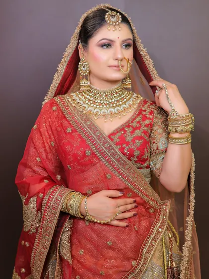 A beautiful bride in a red and gold lehenga with a sheer dupatta. This look is a testament to timeless bridal elegance, available for rent along with the jewellery.