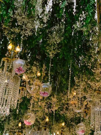 A detailed view of the hanging installation, showing the delicate crystal chains, glass baubles with pink flowers, and the intricate chandeliers nestled within the greenery.